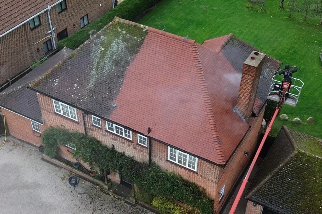 Half-cleaned roof in Fareham showing moss-covered tiles on one side and clean red tiles on the other, with a roof cleaner working from a cherry picker